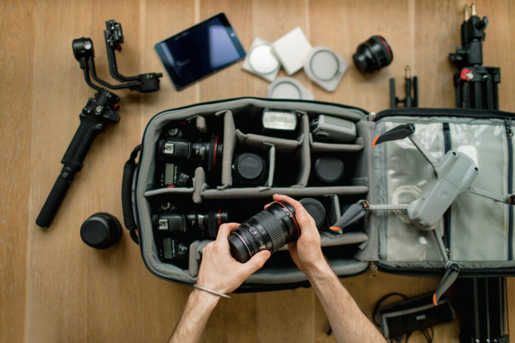 Professional photographer packs smart backpack with equipment, holding lens. Social media influencer top view on suitcase with lens, videocamera and camera, amateur drone and gimbal
